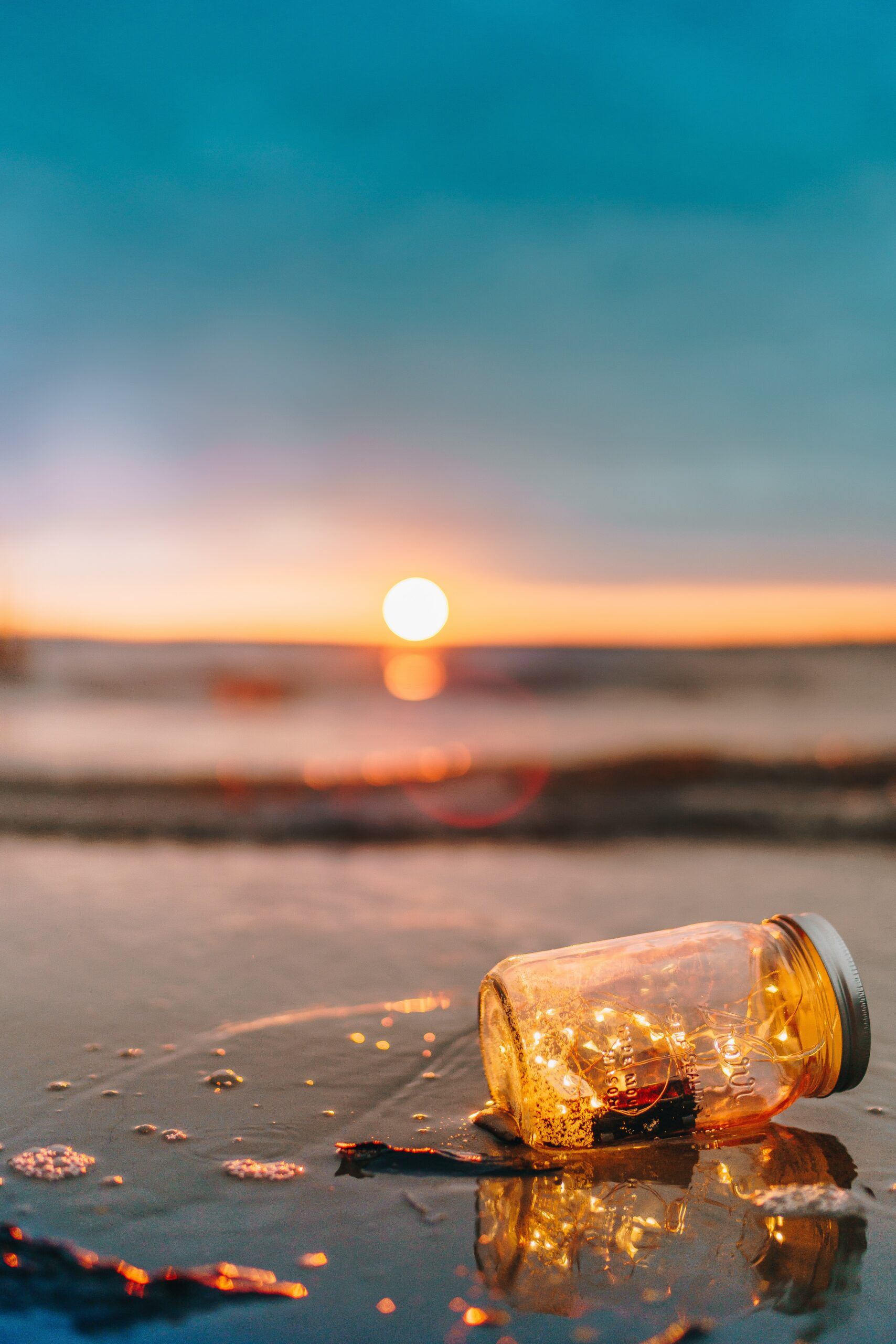 Glas mit Lichterkette am Strand bei Sonnenuntergang